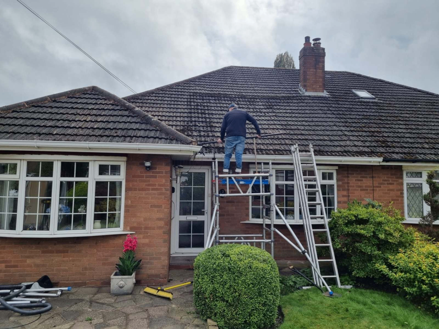 GS Roofs Ltd operative on a scaffold tower cleaning a large tiled roof in Staffordshire